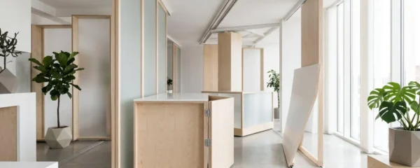 Espace intérieur modulaire avec cloisons mobiles en bois clair et verre dépoli, baigné de lumière naturelle, illustrant un aménagement flexible et reconfigurable